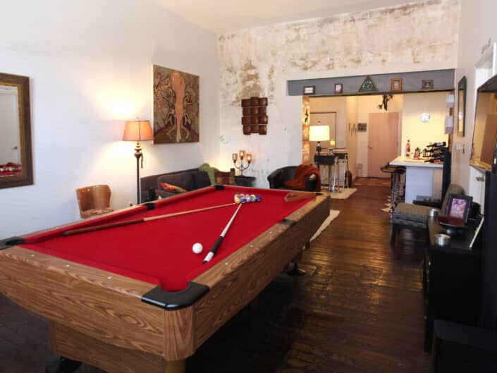 Spacious game room with a red pool table, comfortable lounge area, and eclectic decor on rich wooden flooring