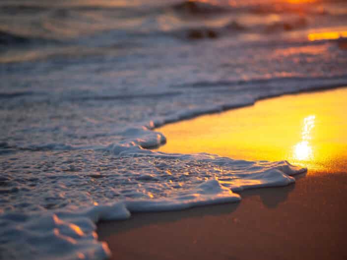 Sunset on the beach with the sun reflecting on wet sand and gentle waves