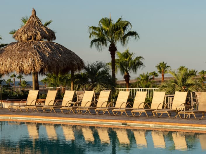Poolside paradise with a thatched cabana and loungers under the tranquil palm trees at sunset