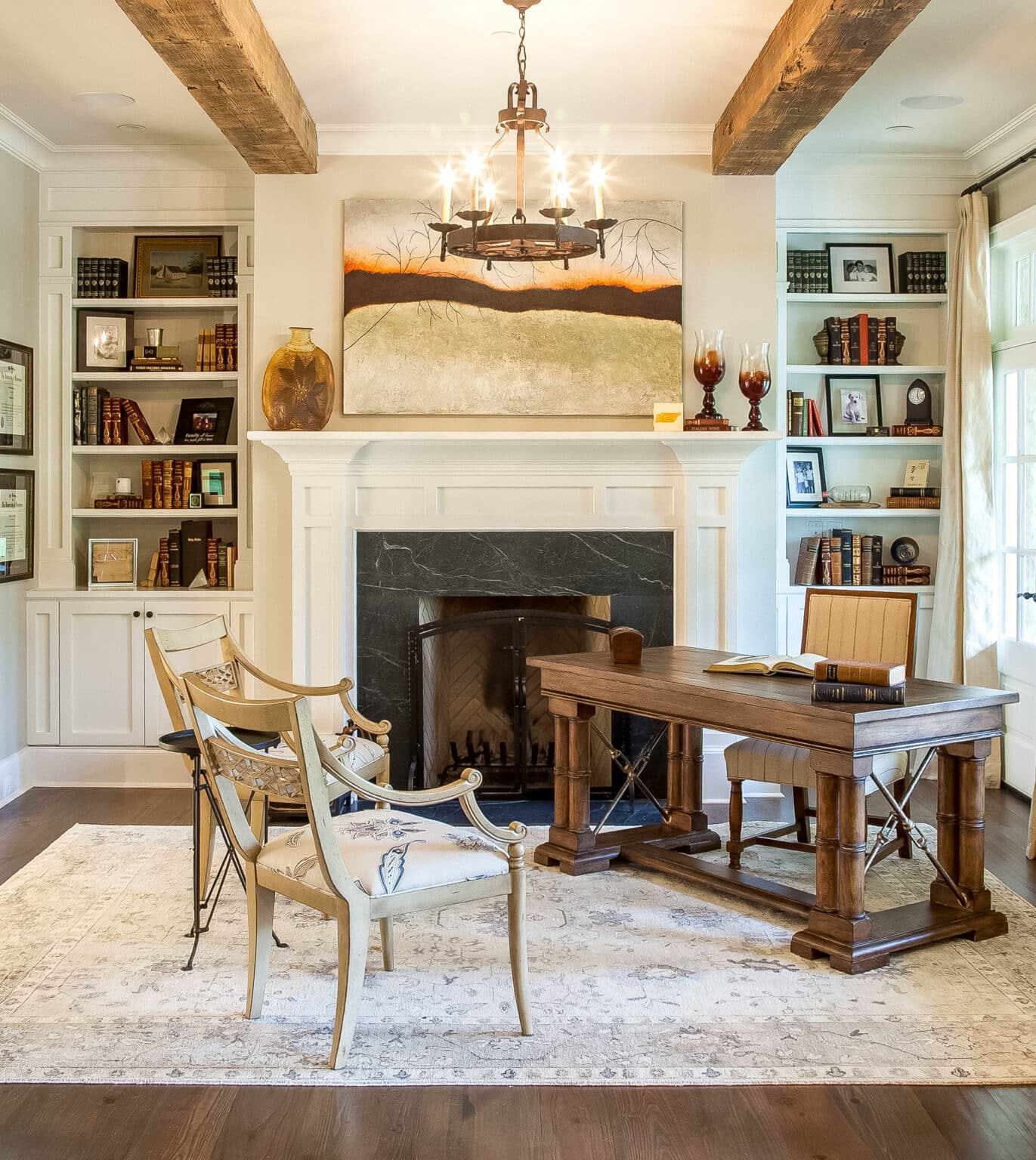 An elegant home office with a traditional wooden desk, classic armchairs, and a fireplace, under a rustic chandelier